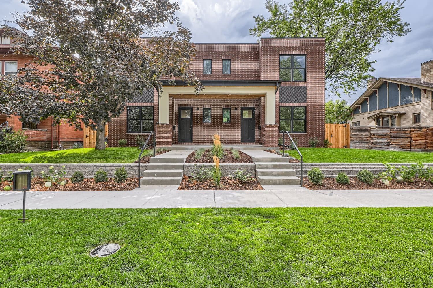 Brick duplex with two covered entries, black-framed windows and a front lawn behind a low retaining wall