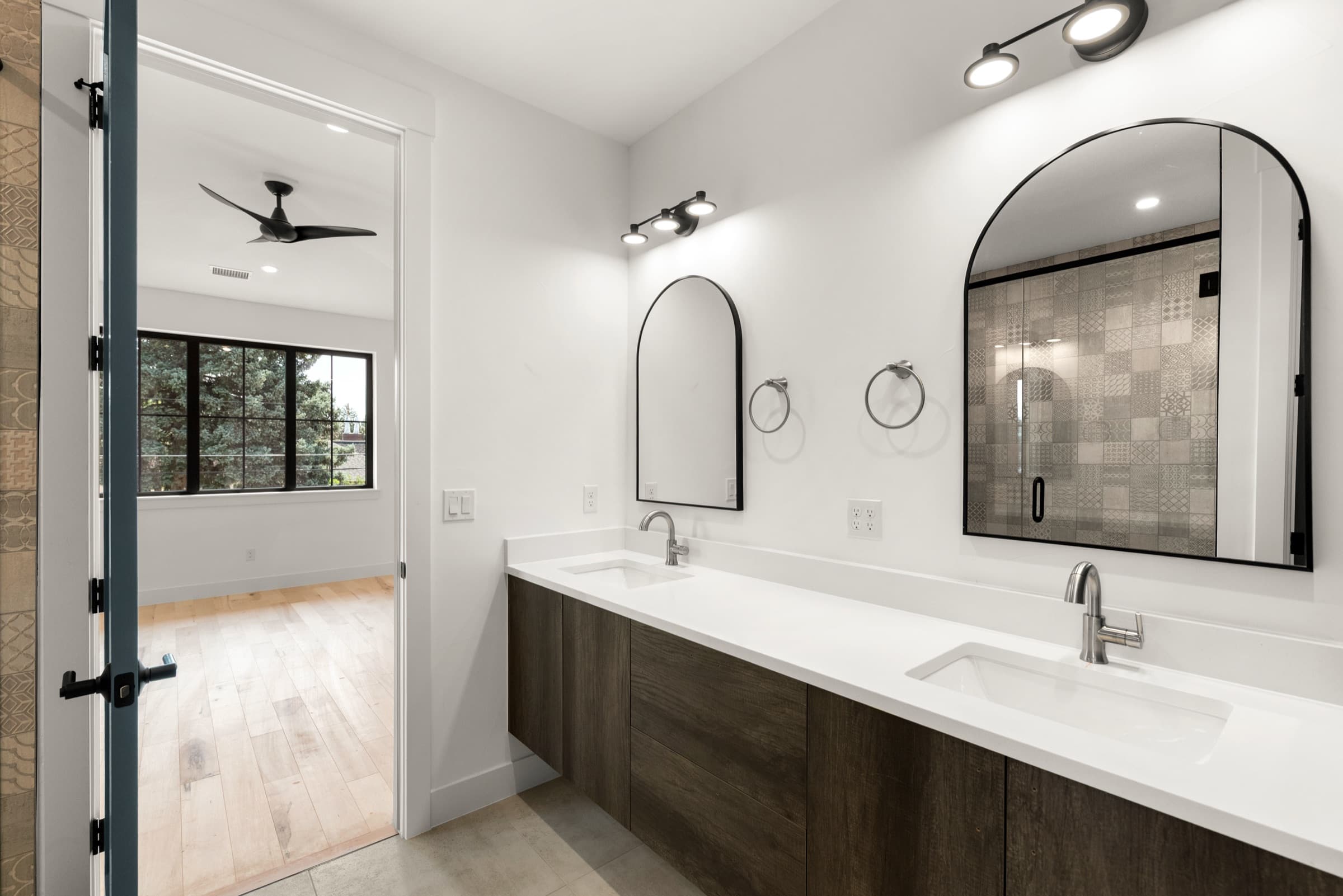 Primary bath with a double vanity, arched mirrors and a patterned tile shower