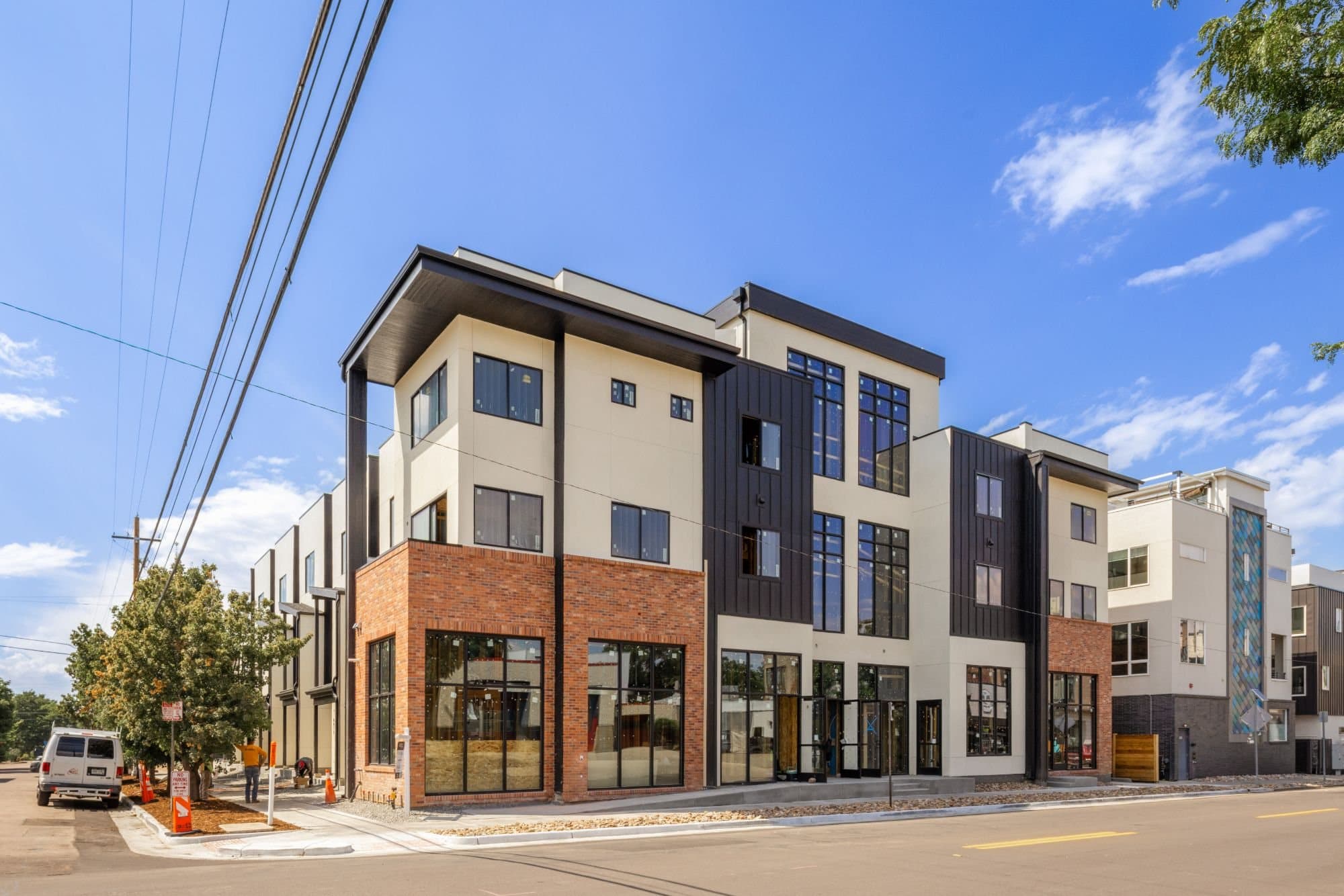 Corner of a mixed-use townhome building in stucco, dark metal panel and brick